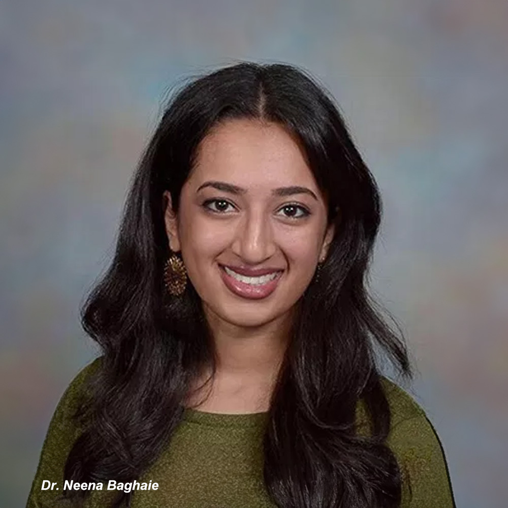 The image features a young woman with dark hair smiling at the camera. She has fair skin and is wearing a green top. Behind her, there s a blue background that appears to be a school setting.